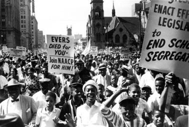 Thousands rally against racial discrimination in downtown Detroit during the “March to Freedom” civil rights demonstration. Signs read “Enact Effective Legislation to End School Segregation,” “Fight for Freedom — Join the NAACP,” and “Evers Died for You — Join the NAACP for Him.” In the background the Fox Theater and St. John’s Episcopalian Church are in view. Courtesy of Walter P. Reuther Library, Wayne State University